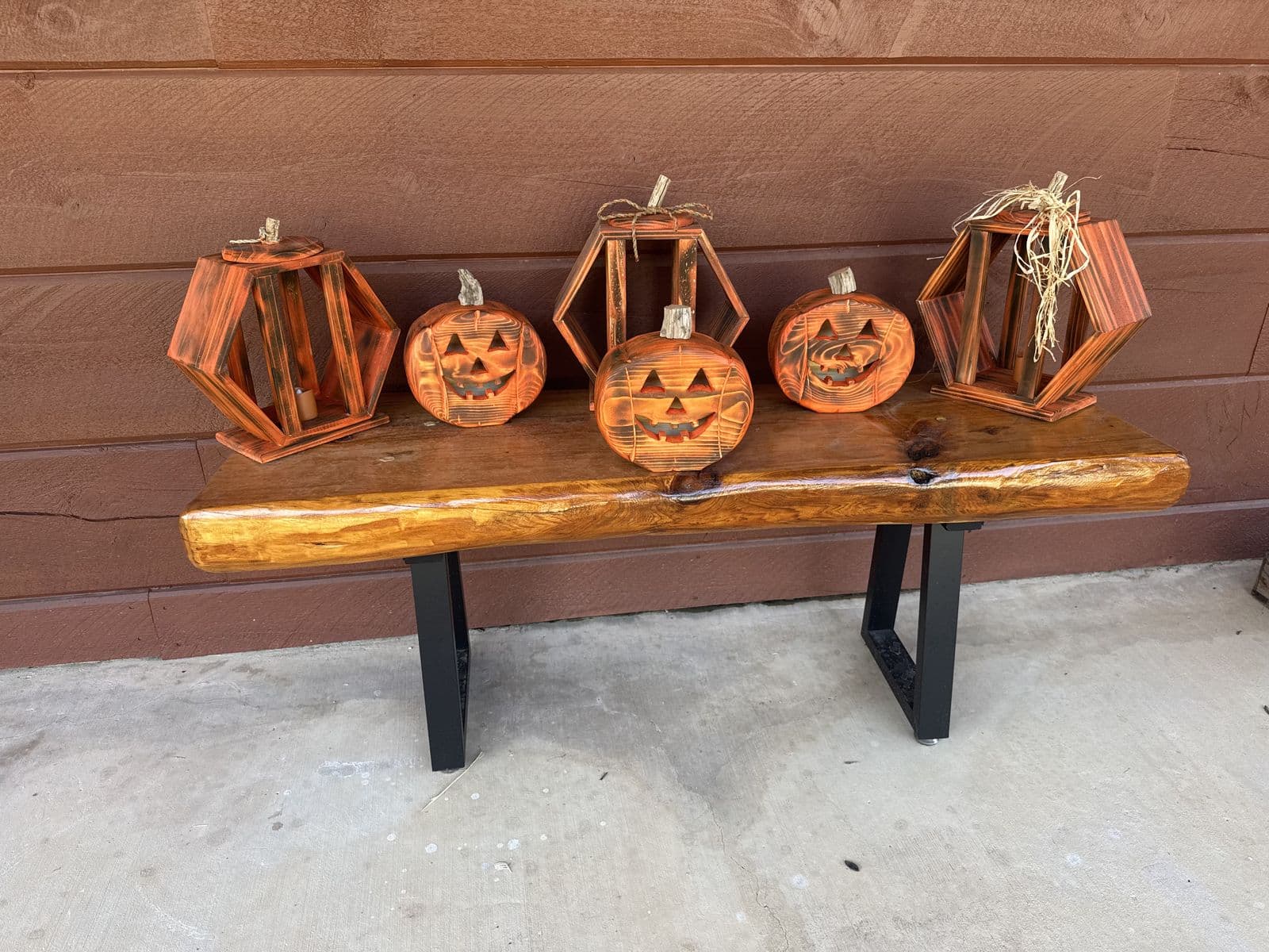 Torched cedar hexagon pumpkin lanterns and carved jack-o'-lanterns on a live-edge bench